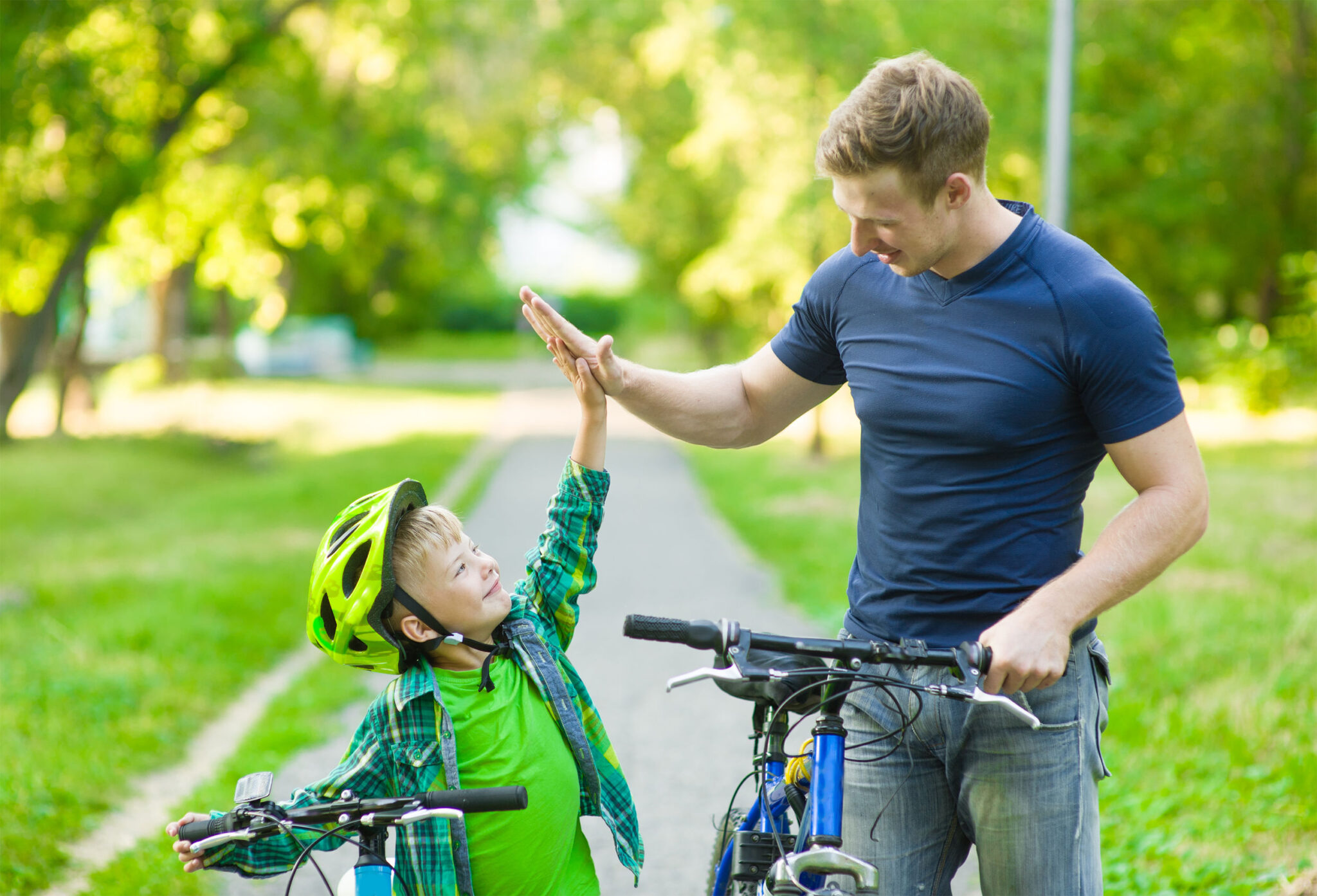 Young man and young boy give high five while cycling in the park