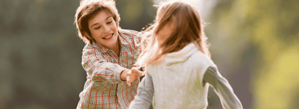 Brother and sister chasing each other in a park