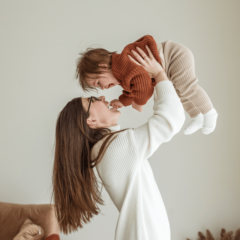 a nanny holding a baby above her head laughing