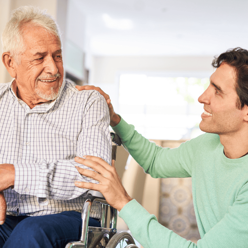 Elderly male companion and old male in wheelchair smiling at eachother