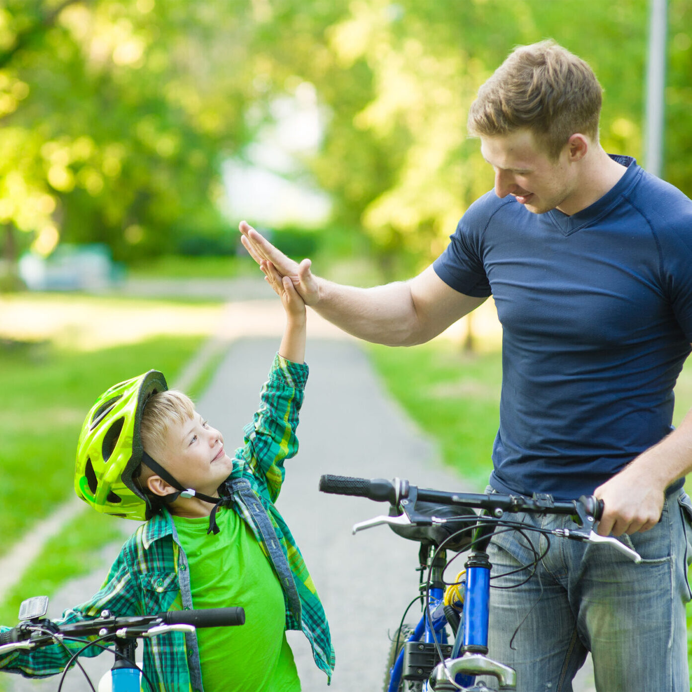 Young man and young boy give high five while cycling in the park